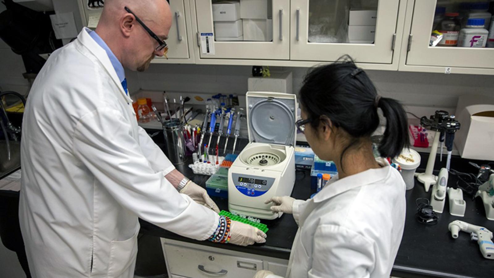 Dr. Baines showing a student the use of benchtop lab equipment.
