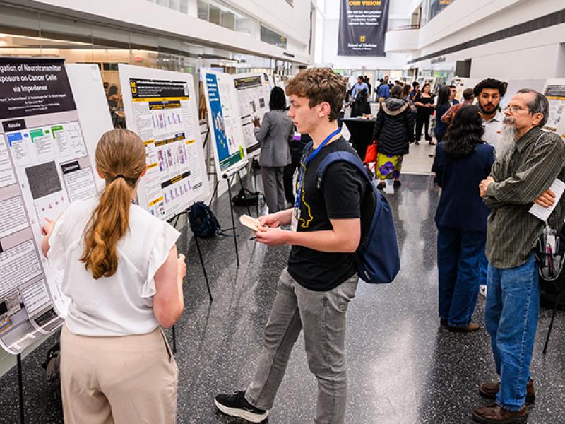 A photo of people reviewing posters during the Cancer Research Day.